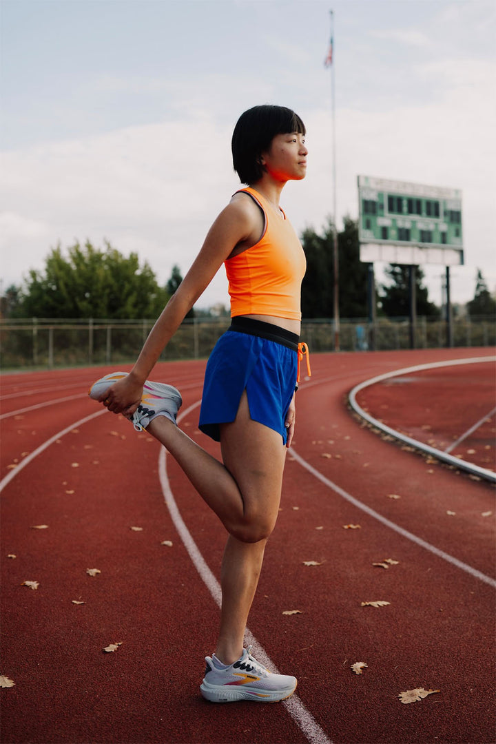 Woman wearing orange SMRc pocket tank and blue running shorts bundle